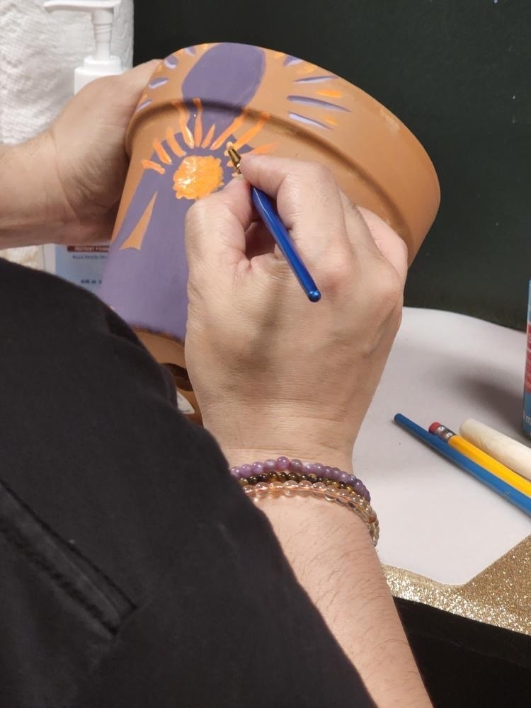 Close-up of hands painting a floral design on a terracotta pot