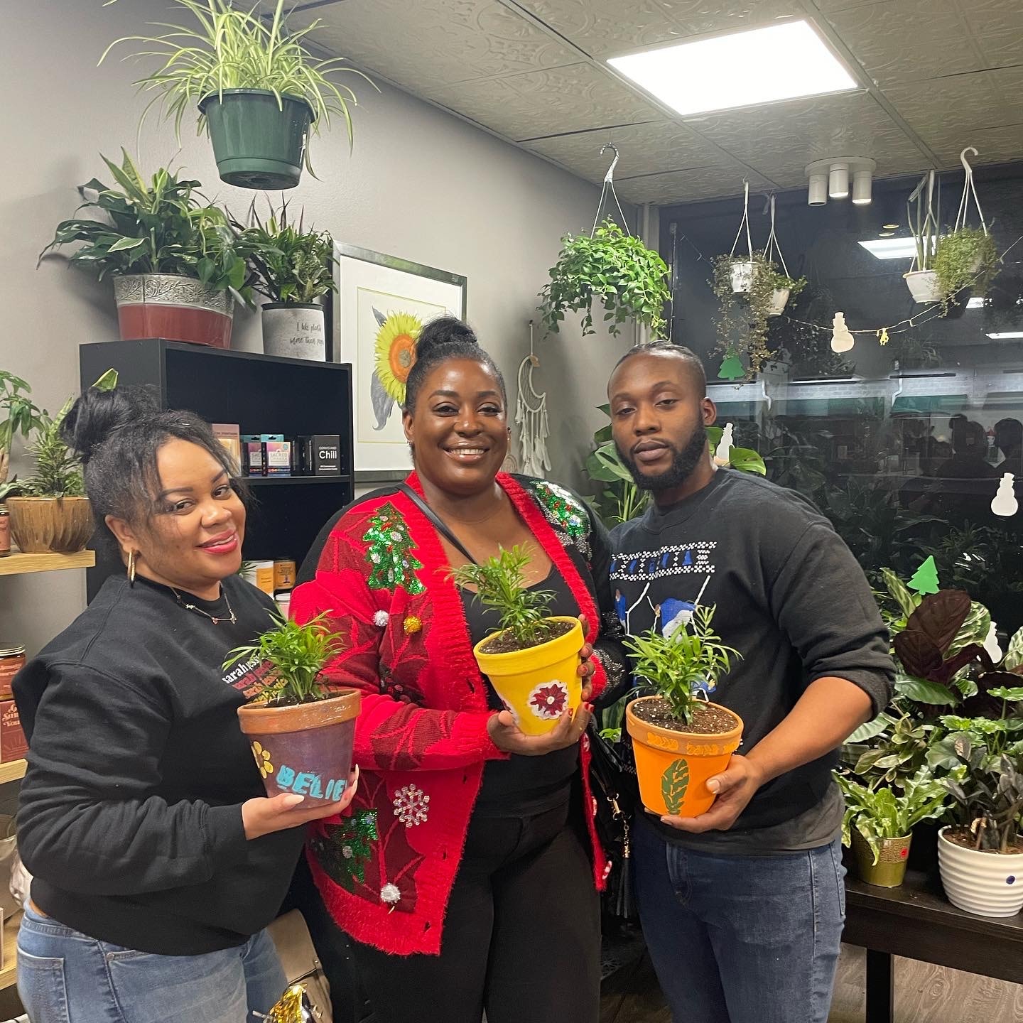 Three workshop participants holding their painted pots in a plant-filled studio