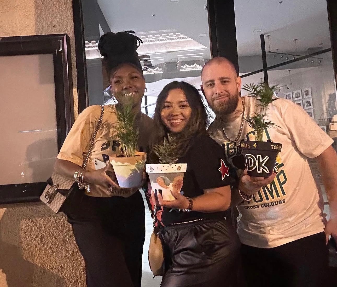 Three workshop participants smiling and holding their painted pots outside at night