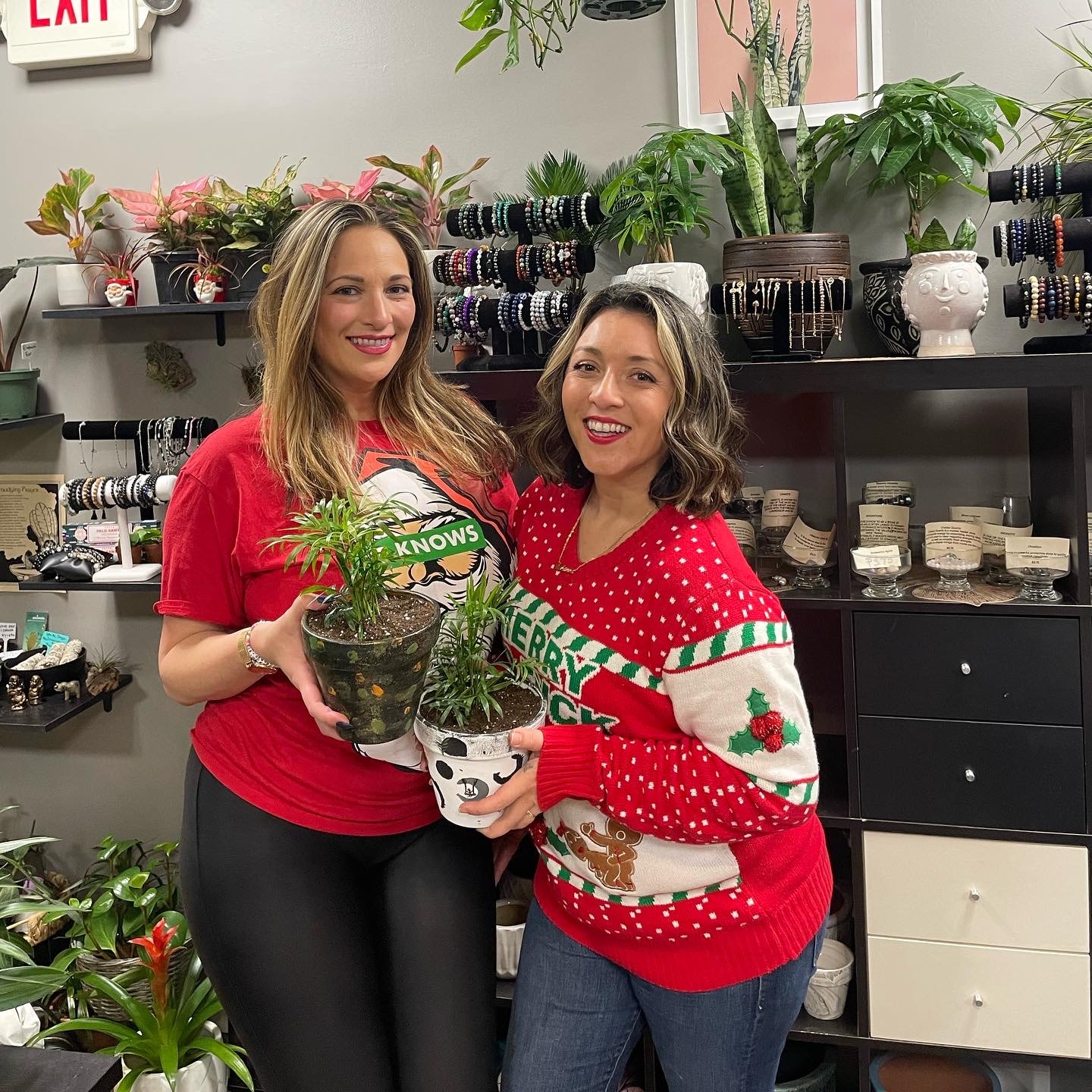 Two women holding their painted pots surrounded by plants and jewelry displays