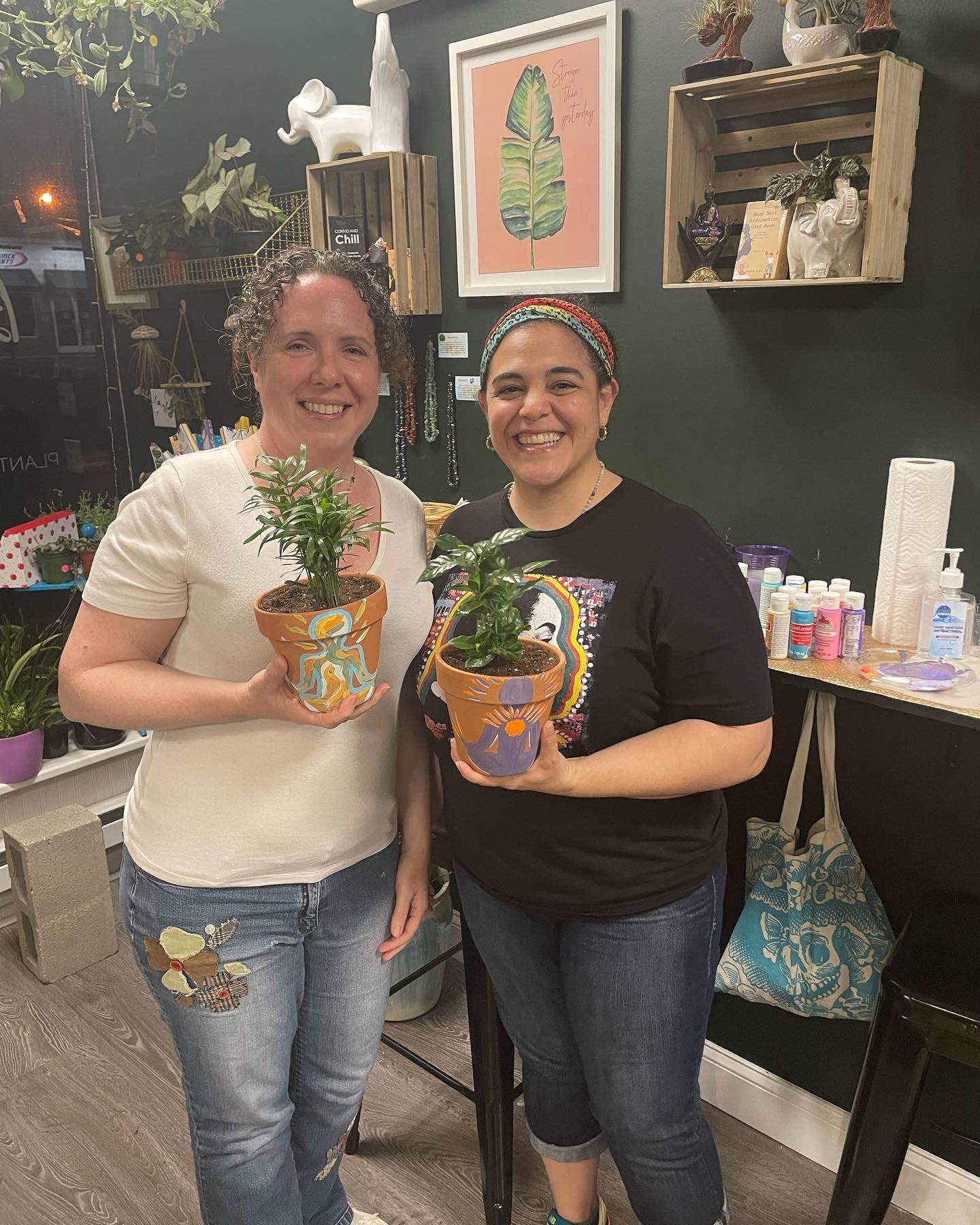 Two women proudly holding their hand-painted pots with plants